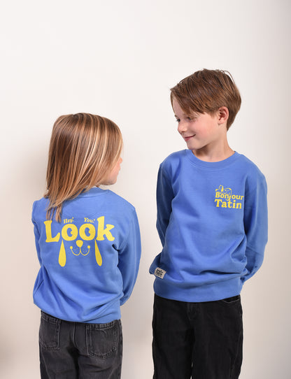 Two children wearing blue sweatshirts with yellow text on a plain background