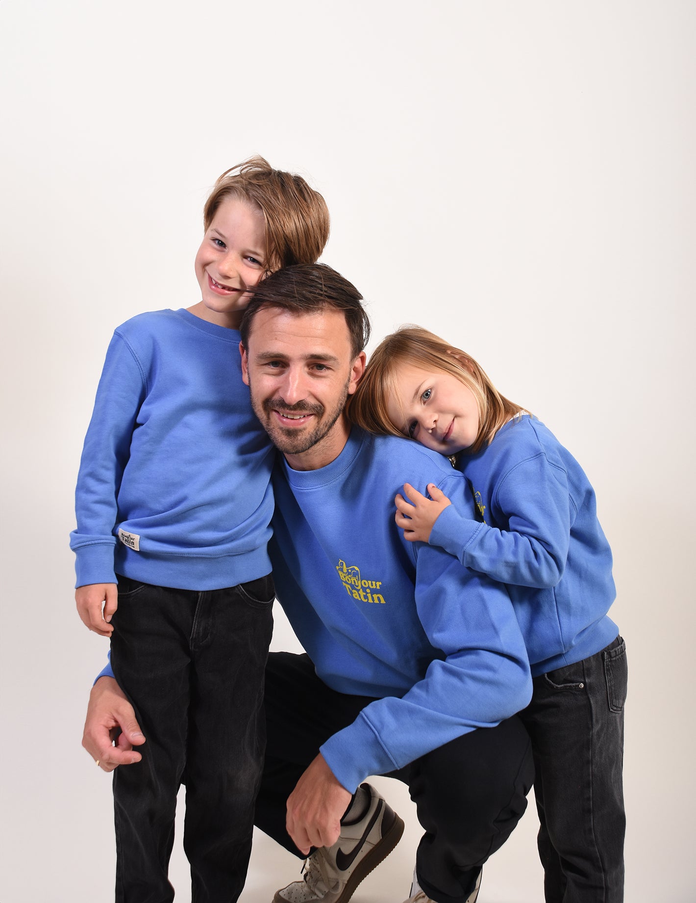 Man with two children wearing matching blue sweatshirts on a white background