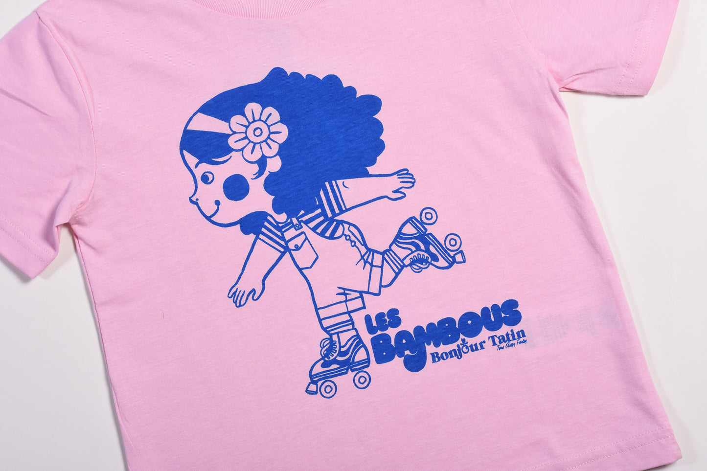 Pink t-shirt with blue graphic of a girl on roller skates and text 'Les Bambous' on a white background