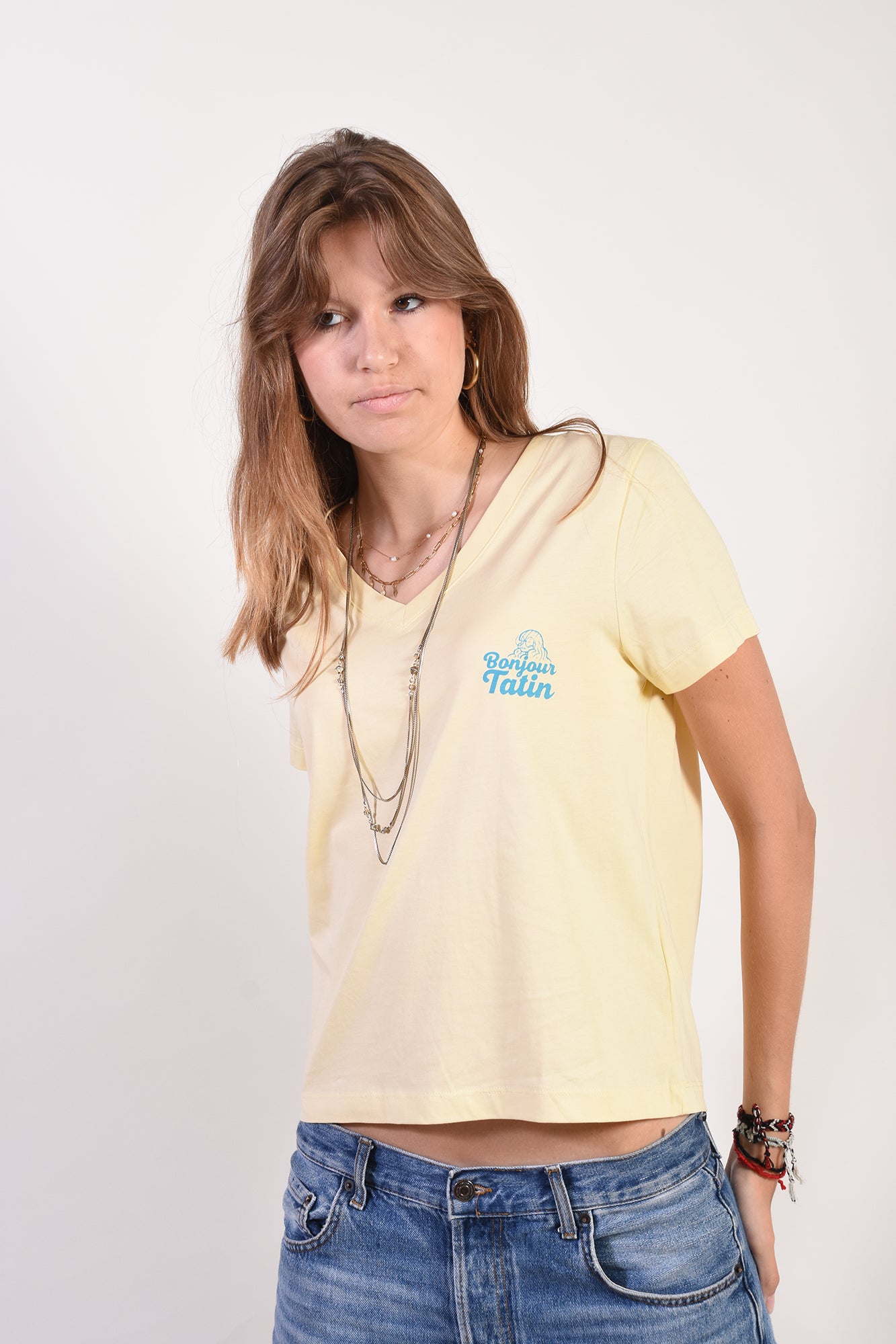Woman wearing a light yellow t-shirt with a logo and blue jeans on a white background