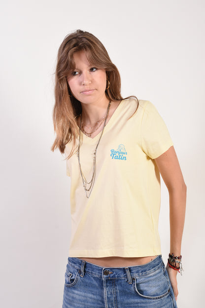 Woman wearing a light yellow t-shirt with a logo and blue jeans on a white background